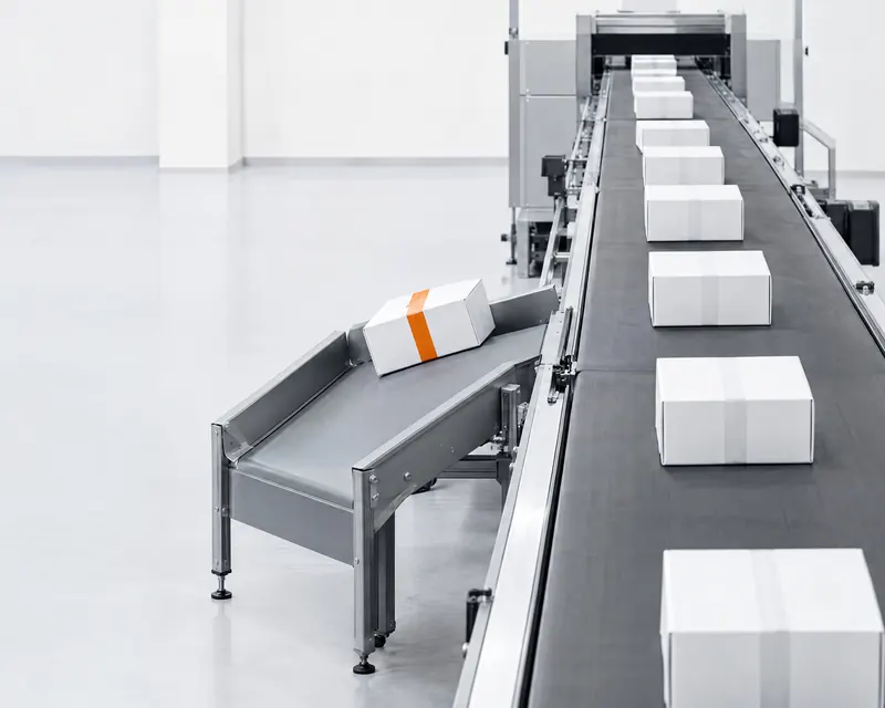 A parcel-sorting line of identical white parcels, one with orange tape turned onto a side lane.