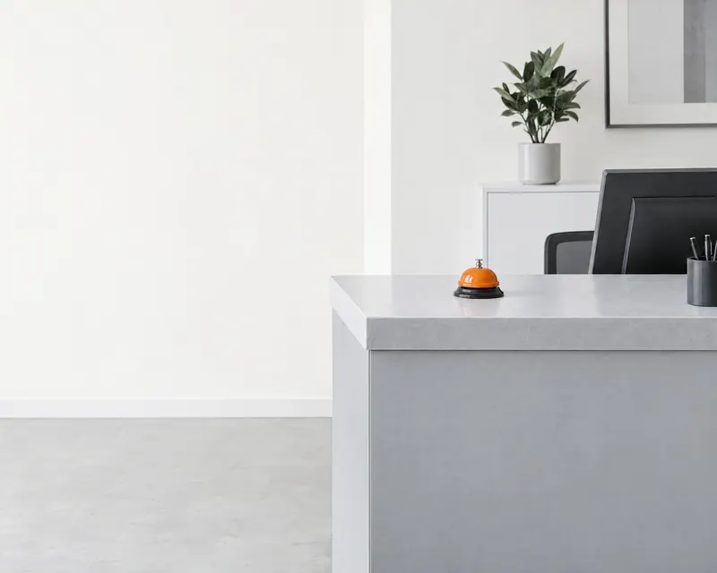 A tidy reception counter seen from the customer’s side, with an orange service bell.